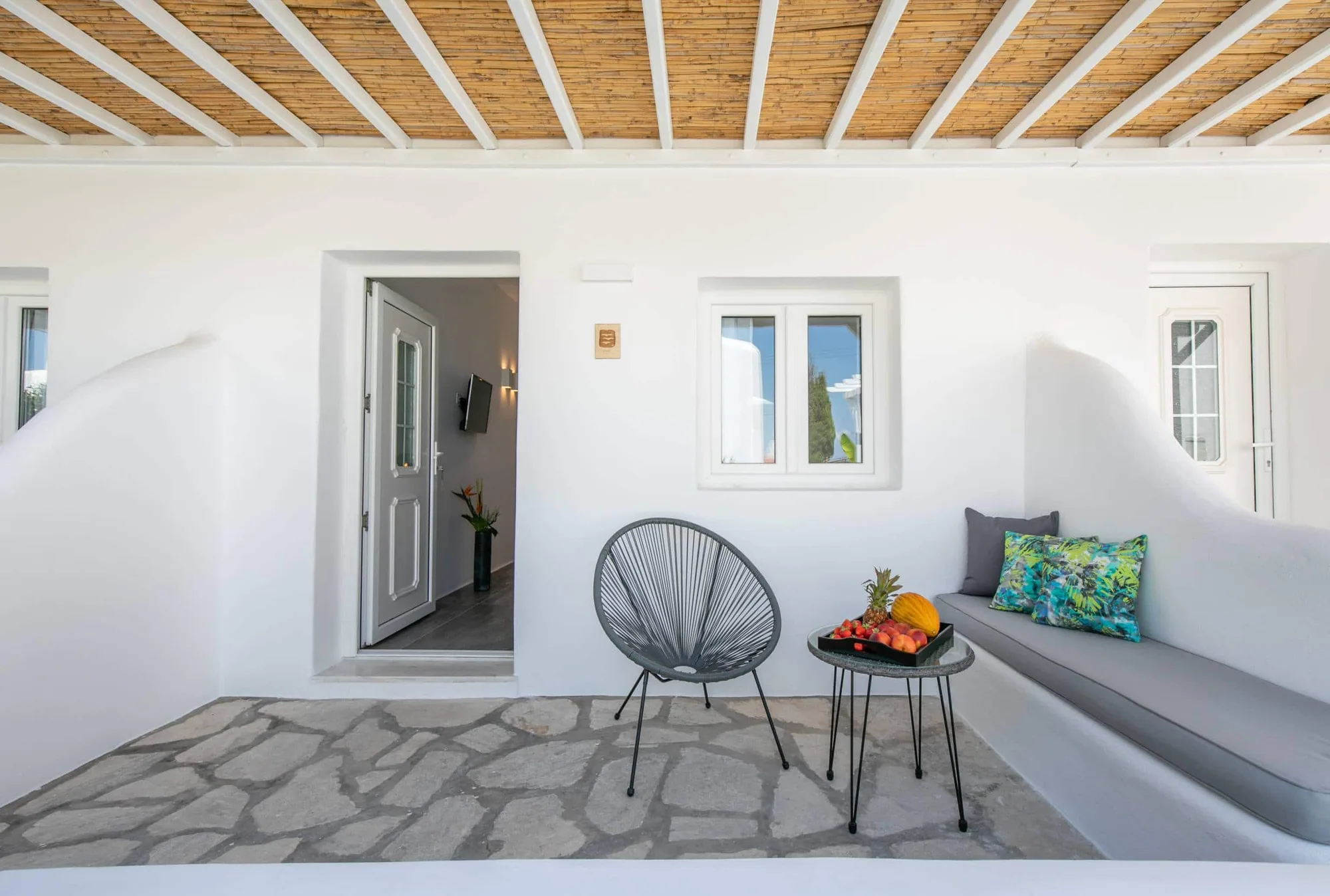 Shaded terrace lounge with grey cushions under a reed ceiling